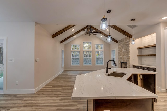 kitchen with sink, light wood-type flooring, lofted ceiling with beams, hanging light fixtures, and a kitchen island with sink