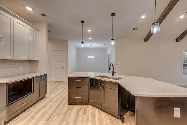 kitchen featuring beam ceiling, a center island with sink, sink, decorative light fixtures, and light wood-type flooring