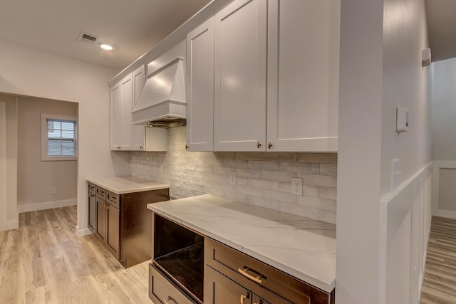 kitchen featuring white cabinets, decorative backsplash, premium range hood, light stone countertops, and light hardwood / wood-style floors