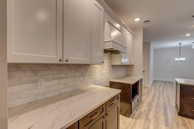 kitchen with light stone countertops, pendant lighting, white cabinetry, premium range hood, and light hardwood / wood-style floors