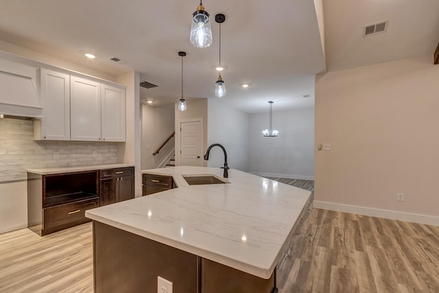 kitchen with tasteful backsplash, sink, light hardwood / wood-style floors, white cabinets, and light stone counters