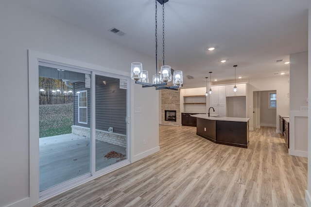 kitchen with an island with sink, light hardwood / wood-style flooring, dark brown cabinetry, pendant lighting, and a fireplace