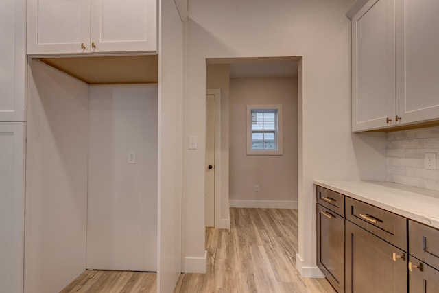 kitchen featuring light hardwood / wood-style flooring, white cabinetry, light stone counters, and backsplash