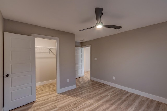 unfurnished bedroom featuring a closet, ceiling fan, light hardwood / wood-style floors, and a walk in closet