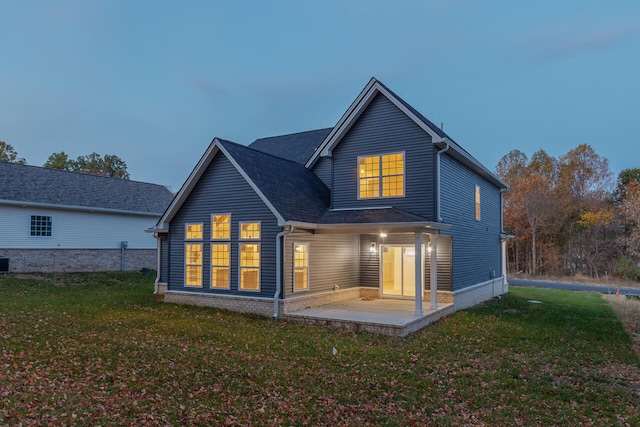 back house at dusk with a yard, a patio, and central air condition unit