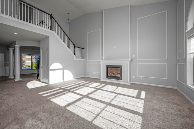 unfurnished living room with high vaulted ceiling, decorative columns, and carpet floors