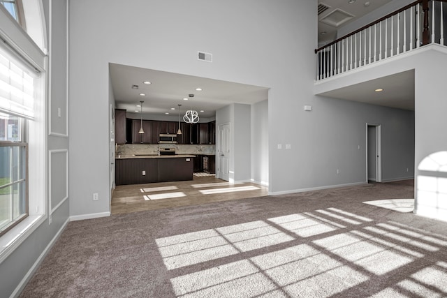 unfurnished living room with carpet, a notable chandelier, and a towering ceiling