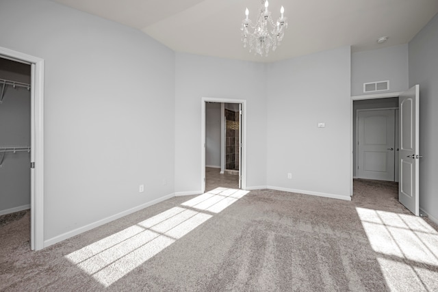 unfurnished bedroom with a closet, a chandelier, light colored carpet, and a walk in closet