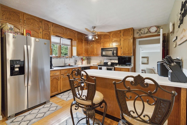 kitchen with tasteful backsplash, sink, ceiling fan, stainless steel appliances, and light hardwood / wood-style flooring