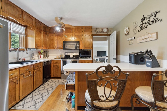 kitchen with black appliances, sink, light wood-type flooring, decorative backsplash, and a breakfast bar