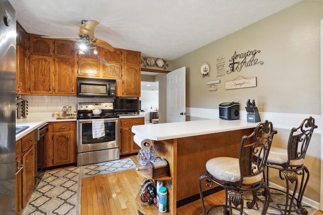 kitchen featuring light hardwood / wood-style floors, black appliances, a breakfast bar, and kitchen peninsula