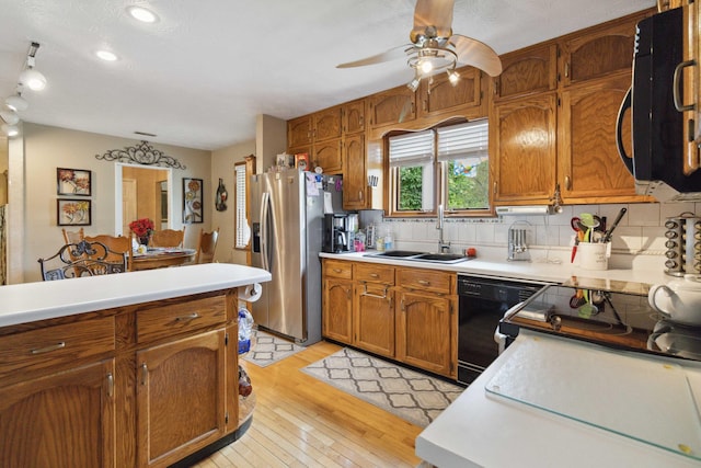 kitchen featuring black dishwasher, stainless steel refrigerator with ice dispenser, backsplash, sink, and light wood-type flooring