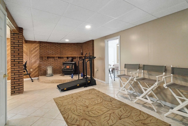 workout area featuring a paneled ceiling, tile patterned floors, and a wood stove