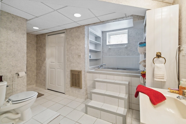 bathroom featuring a tub to relax in, a paneled ceiling, toilet, and tile patterned flooring