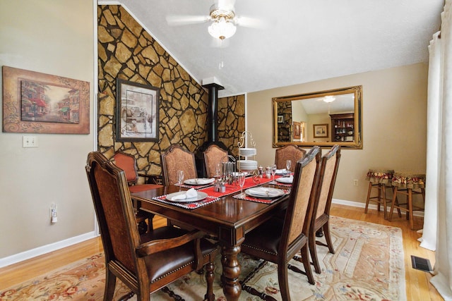 dining room featuring light hardwood / wood-style floors, lofted ceiling, a wood stove, and ceiling fan