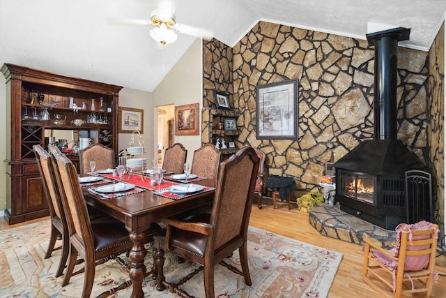 dining room with lofted ceiling, light hardwood / wood-style flooring, a wood stove, and ceiling fan