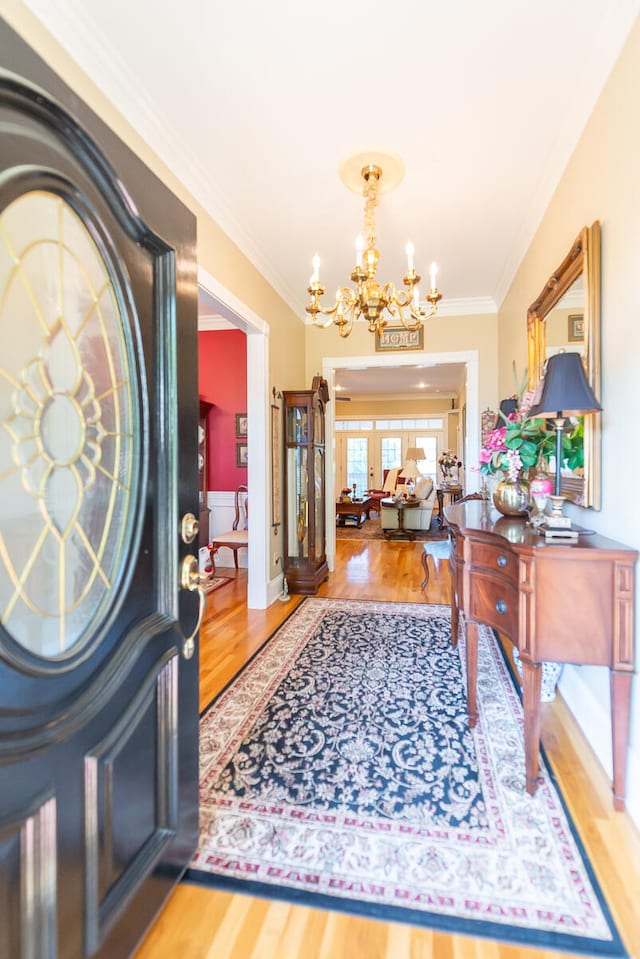 foyer entrance with ornamental molding, wood-type flooring, and a chandelier