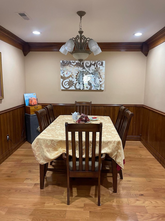 dining area with ornamental molding, a chandelier, light wood-type flooring, and wooden walls