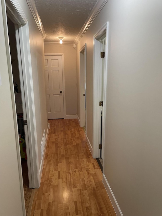 hallway featuring ornamental molding, a textured ceiling, and light wood-type flooring