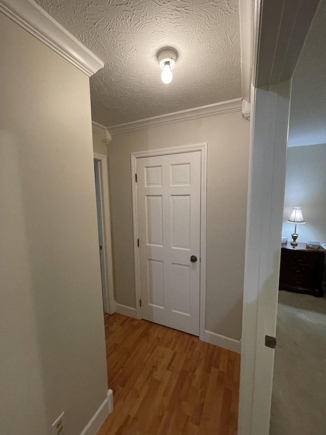 hall with ornamental molding, light hardwood / wood-style floors, and a textured ceiling