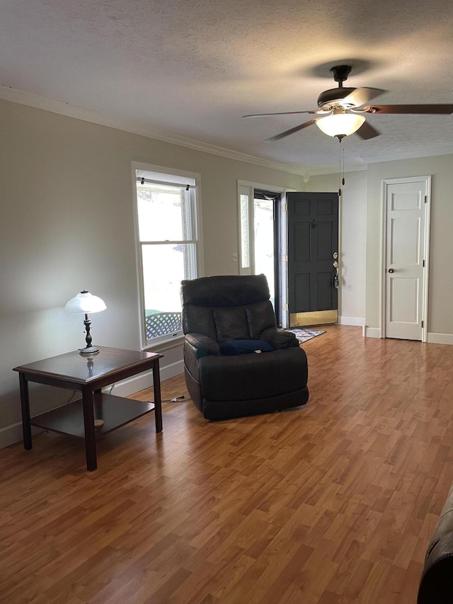 living room featuring ceiling fan, crown molding, wood-type flooring, and a textured ceiling