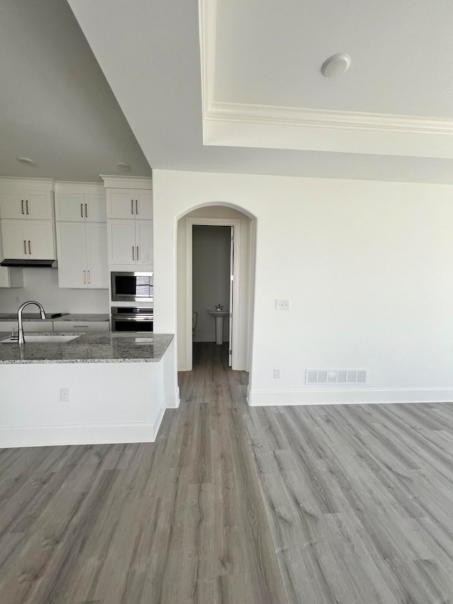 kitchen with white cabinets, appliances with stainless steel finishes, light wood-type flooring, dark stone countertops, and sink