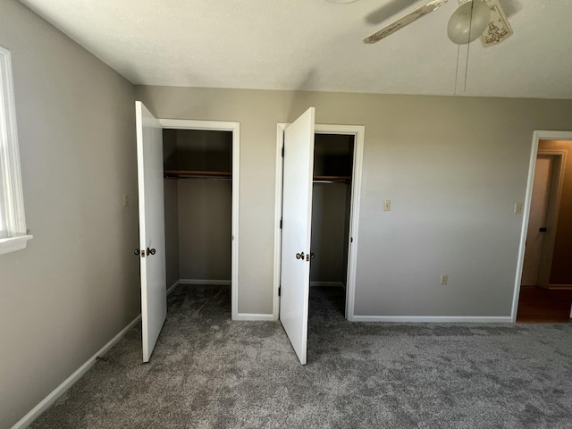 unfurnished bedroom with ceiling fan, dark carpet, and multiple closets