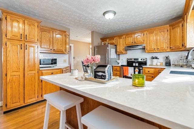 kitchen with light hardwood / wood-style flooring, sink, stainless steel appliances, decorative backsplash, and a breakfast bar