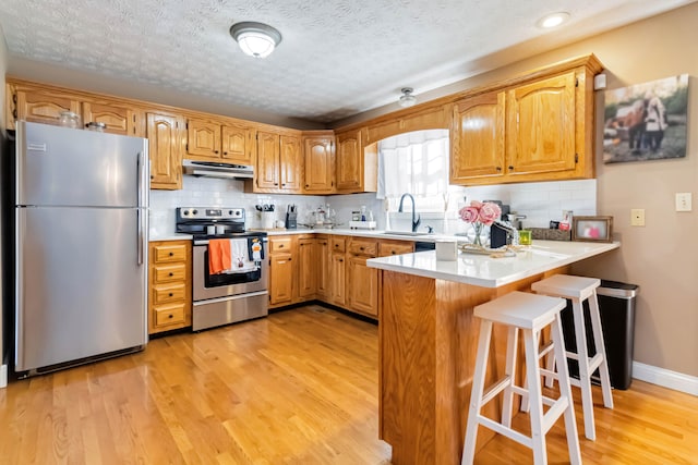 kitchen featuring light wood-type flooring, appliances with stainless steel finishes, kitchen peninsula, and a kitchen bar