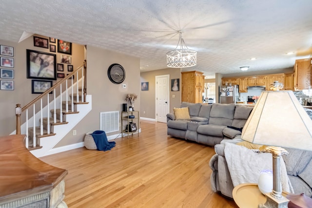 living room featuring an inviting chandelier, a textured ceiling, and light wood-type flooring