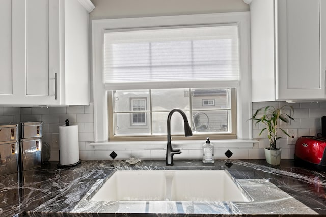 details featuring white cabinetry, dark stone countertops, tasteful backsplash, and sink