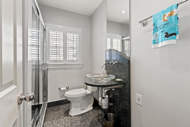 bathroom featuring toilet, a shower with shower door, and sink