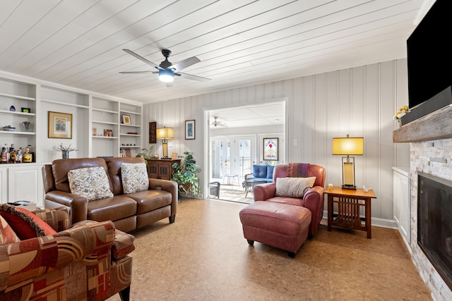 living room featuring a stone fireplace, ceiling fan, wooden ceiling, and built in shelves