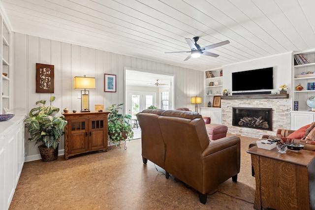 living room with a stone fireplace, built in features, ceiling fan, wooden ceiling, and ornamental molding