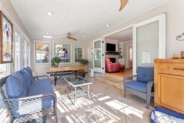 sunroom with ceiling fan and a stone fireplace