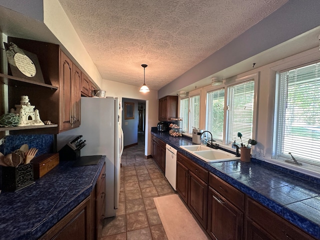 kitchen featuring hanging light fixtures, light tile patterned floors, a textured ceiling, dishwasher, and sink