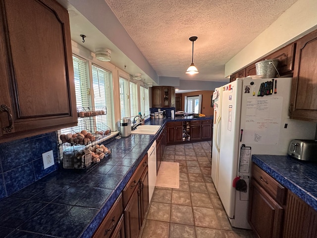 kitchen featuring sink, light tile patterned flooring, decorative light fixtures, a textured ceiling, and white appliances