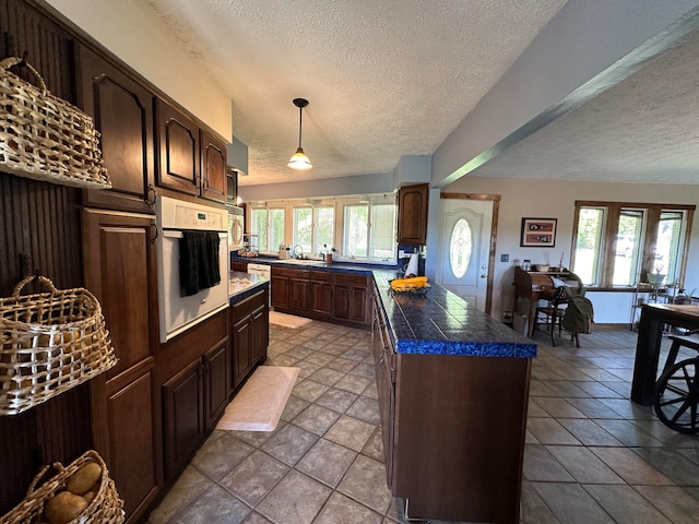 kitchen featuring oven, a textured ceiling, a healthy amount of sunlight, and dark brown cabinetry