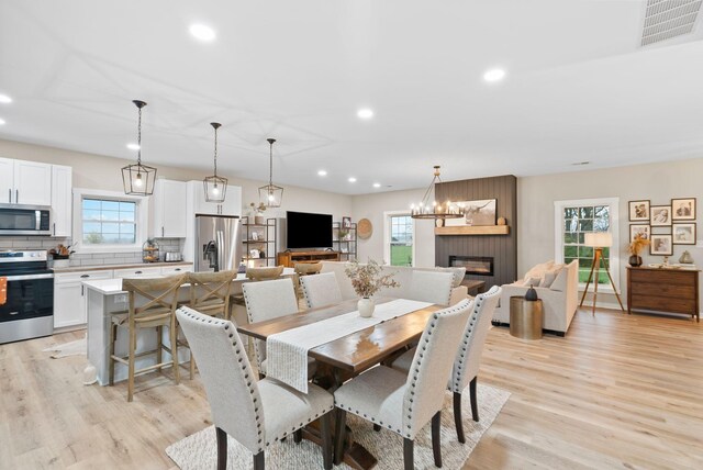 dining room with light wood-type flooring, a large fireplace, visible vents, and a healthy amount of sunlight