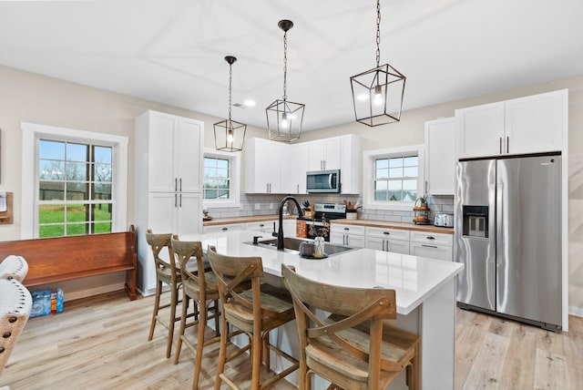 kitchen featuring a breakfast bar, tasteful backsplash, appliances with stainless steel finishes, light wood-style floors, and a sink