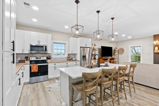 kitchen with tasteful backsplash, visible vents, white cabinets, appliances with stainless steel finishes, and light wood-type flooring