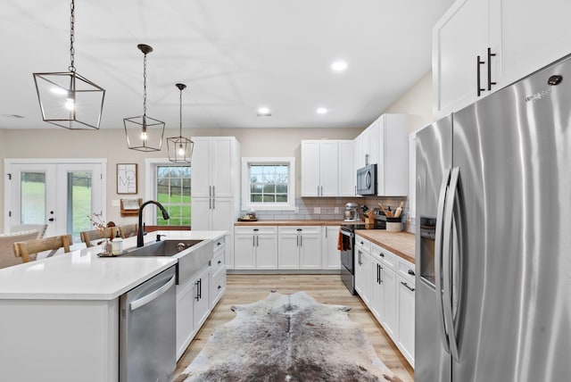 kitchen featuring decorative backsplash, stainless steel appliances, french doors, light wood-style floors, and a sink