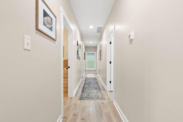 corridor with light wood-type flooring, visible vents, and baseboards