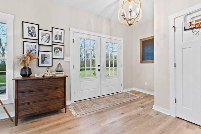 foyer with light wood-style floors, french doors, baseboards, and an inviting chandelier