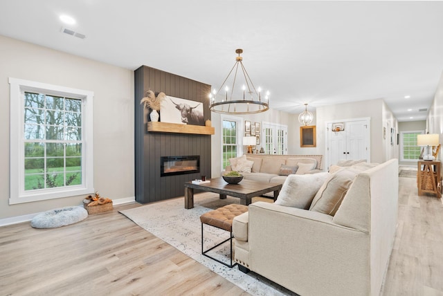 living area featuring visible vents, a large fireplace, wood finished floors, a chandelier, and baseboards