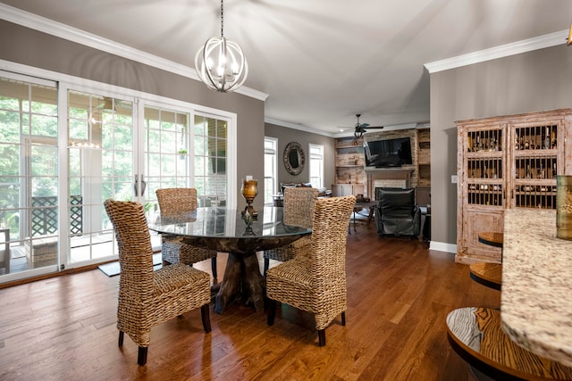 dining space featuring ornamental molding, dark wood-type flooring, a fireplace, and ceiling fan with notable chandelier