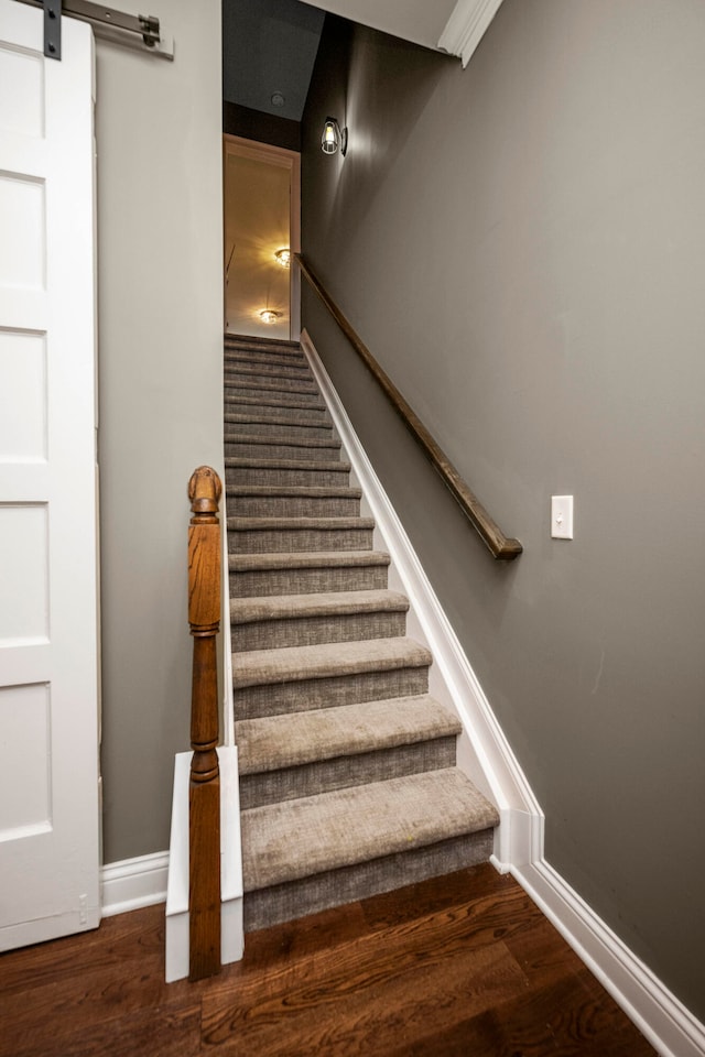 staircase with a barn door and wood-type flooring