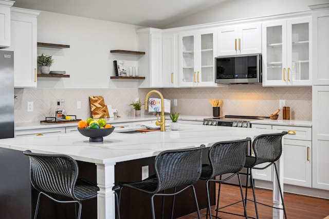 kitchen featuring white cabinetry, light stone countertops, stainless steel appliances, and a kitchen bar