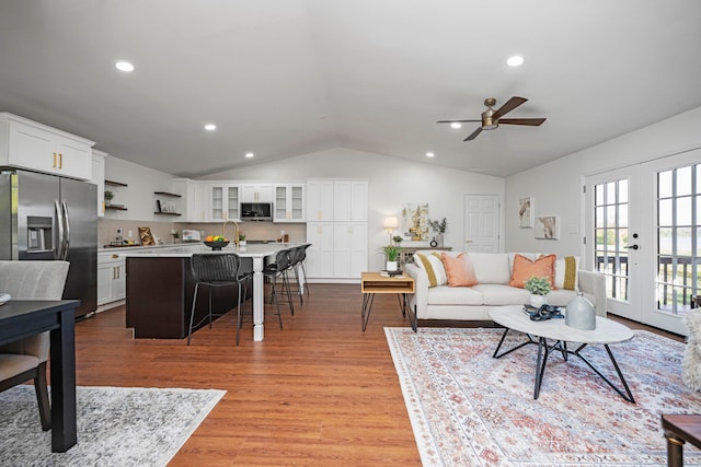 living room with ceiling fan, vaulted ceiling, light hardwood / wood-style flooring, french doors, and sink