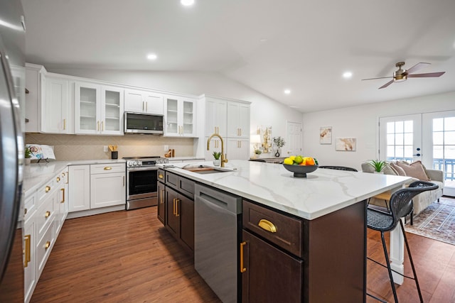 kitchen with an island with sink, appliances with stainless steel finishes, vaulted ceiling, dark wood-type flooring, and sink